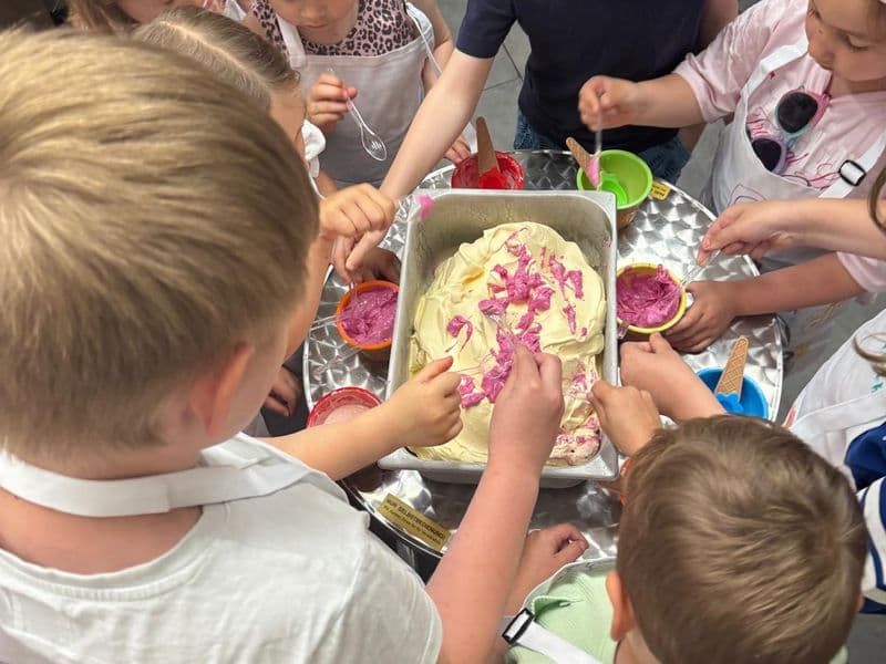 Kinder rühren an einem Metallbecken bunte Eiscreme an